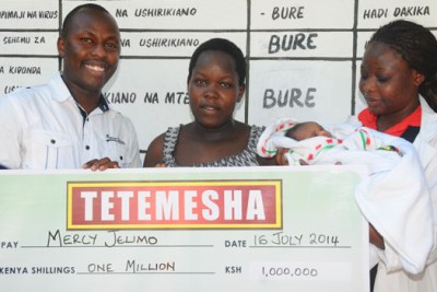 Mercy Jelimo holding her cheque from Safaricom together with her newborn baby.
