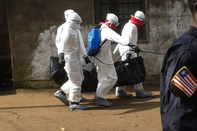 The burial team carries the body of a suspected Ebola victim under the watchful eyes of police officers.