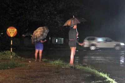 Women stand along the Avenues in Harare at night.