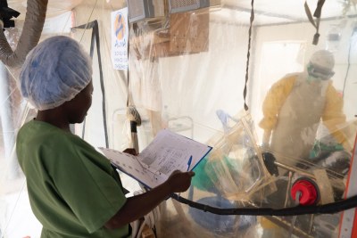 Health workers talk to an Ebola patient, while a nurse consults a chart outside at an Ebola treatment centre in Beni, Democratic Republic of the Congo.