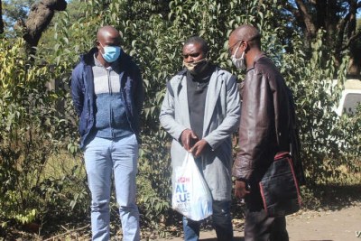 Journalists Samuel Takawira and Frank Chikowore stand with a police detective outside a court in Harare, Zimbabwe, May 23, 2020.