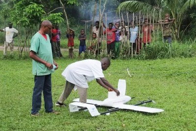 A drone carrying vaccines arrives at Widjifake Health Center where health workers, Emmanuel and Fabrice, unload the package.